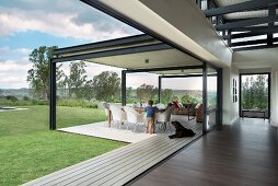 White designer chairs around table on roofed terrace of architect-designed house; child and dog in front of table