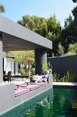 Pond outside modern house with roofed terrace painted grey and comfortable floor cushions on edge