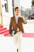 A young businessman wearing a brown blazer and light trousers walking down the road