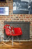 Classic red rocking chair and grey-painted radiator below pictures on brick wall