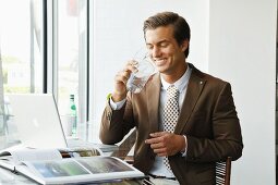 Junger Geschäftsmann mit braunem Sakko sitzt im Büro und trinkt Wasser