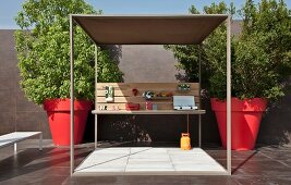 Terrace with cubic pergola flanked by trees in red, oversized plant pots in courtyard