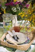 Glasses, jug of water and plates on basket tray outdoors