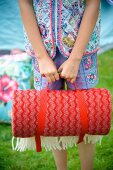 Mädchenhände mit aufgerollter roter Picknickdecke im Garten