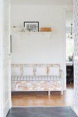 View through open door of shabby-chic bench and picture on white bracket shelf