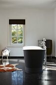 Free-standing vintage bathtub, standpipe tap fittings, large black floor tiles and cowhide rug in minimalist bathroom