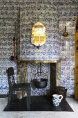 Cooking pot hanging in open fireplace with entire chimney breast and wall tiled with old Delft tiles; postmodern metal chair with perforated structure in foreground