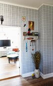 Hallway with tartan wallpaper and floor vase below bracket shelf next to open living room door