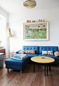 Round coffee table with yellow top, blue sofa with matching ottoman and picture on wall in simple living room