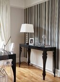 Postmodern, black console table and table lamp with white lampshade against wall with striped wallpaper in various shades of grey