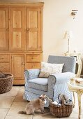 Comfortable armchair with striped cover next to knitting basket and cat sitting on floor