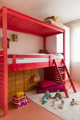 Hochbett aus hellrot gebeiztem Holzgestell mit Leiter, davor Spielsachen auf Teppich, im Kinderzimmer