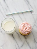 A rose cupcake with a glass of milk