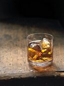 A glass of whiskey over ice on a wooden table