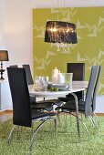 Pendant lamp with black fabric lampshade above chairs with black leather covers, oval dining table and rug; large artwork with bird motif on wall