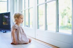 Kleines Mädchen sitzt auf Boden vor Terrassentür
