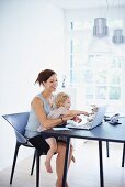 Mother working on notebook with daughter on lap