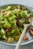 Sliced rhubarb in a baking dish with a wooden spoon