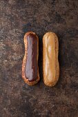 Two éclairs one with chocolate glaze and one with coffee glaze on a baking tray