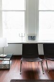 Stuhl aus Metall und Leder vor Altbaufenstern; daneben ein Glastisch mit Tischleuchte