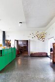 Artwork in corner of loft interior, acoustic fleece on ceiling and old laboratory cabinet with green doors in front of kitchen counter