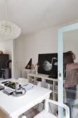 White dining table set with Oriental dishes and woman standing in front of vintage, glass-fronted cabinet