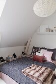 Double bed with blanket and arranged scatter cushions below sloping ceiling