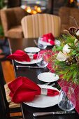 Festlich gedeckter Weihnachtstisch mit weihnachtlichem Gesteck in der Tischmitte; im Hintergrund das Feuer im offenen Kamin