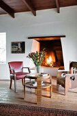 Chair, armchair and round table in front of open fire in rustic, eclectic interior