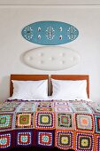 Bett mit weissen Kissen und Patchwork Tagesdecke, Wanddekoration über Holzkopfteil