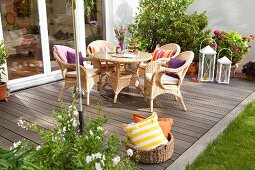 Gemütlicher Sitzplatz mit Rattanmöbeln auf selbstgebauter Holzterrasse, im Vordergrund Korb mit Kissen