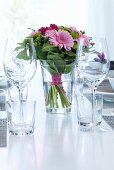 Bouquet of pink flowers, wine glasses and water glasses on festively set table