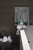 Towels on edge of bathtub below modern artwork on tiled wall