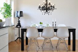 Classic chairs with white shell seats on metal frames around black dining table below chandelier in modern dining room