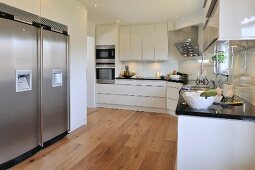 White designer kitchen with wooden floor and stainless steel fridge-freezer in niche