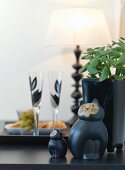Ceramic cats and potted plant on black worksurface with glasses of sparkling wine in background