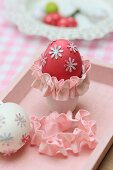 Rot gefärbtes Ei mit Blütenmotiven und rosafarbener Bordüre in Eierbecher