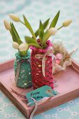White tulips in bottles with hand-crocheted covers on pink tray with Easter greetings on tag