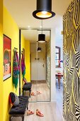 Mirrored wardrobe and antique upholstered bench in hallway with one yellow wall and wallpaper with graphic pattern