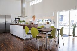 Dining table, green retro chairs and counter in elegant, open-plan kitchen with walnut parquet floor