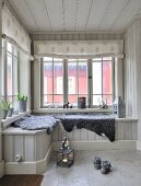 Grey sheepskin blankets on window seat in wood-clad conservatory with fabric roller blinds on lattice windows