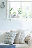 Sofa with scatter cushions in various shades of cream below window in wall painted pastel blue
