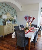 Table set for Christmas dinner, dark wicker chairs and pale sideboard in niche with floral wallpaper
