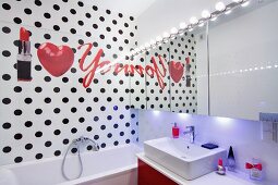 Writing, heart and lipstick on bathroom wall with black polka-dots and mirrored wall with row of spotlight above sink