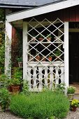 Gartenhäuschen mit Veranda, hinter weißem Holzgitter Blumentöpfe auf Regalböden