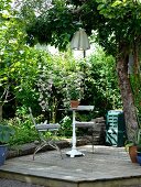 Vintage Bistrotisch und Klappstuhl auf Holzdeck in sommerlichem Garten