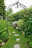 Metal trellis arch over grass path with stepping stones in garden