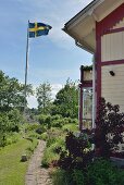 Gepflasterter Gartenweg an weißem Holzhaus vorbeiführend und Fahnenmast mit schwedischer Flagge