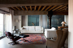 Lounge area with classic armchair and white, modern sofa set in loft-apartment living area with rustic, wood-beamed ceiling