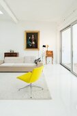 Yellow swivel chair, pale designer sofa, small, antique cabinet and gilt-framed painting on wall in minimalist loft apartment